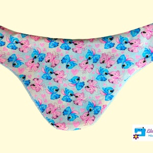 Peut inclure: Un sous-vêtement à motif bleu clair et rose avec des personnages de dessins animés et des cœurs. Le sous-vêtement présente un motif répétitif de personnages bleus et roses avec des cœurs roses sur un fond bleu clair. Les bords sont finis avec une bordure bleu clair.