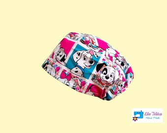 Può includere: Un berretto chirurgico rosa e blu con un motivo di cuccioli dalmata. Il berretto ha un bordo bianco e il testo "Lilo Telitas Hand Made" è stampato in basso a destra.