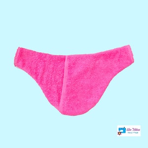 K&ouml;nnte beinhalten: Ein rosa Frottee-Haarband mit einer Naht auf der R&uuml;ckseite. Das Haarband ist so konzipiert, dass es um den Kopf getragen wird und eine gebogene Form hat, um sich bequem an den Kopf anzupassen.