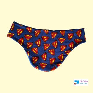 Peut inclure: Bavoir en tissu bleu avec un motif de logo Superman. Le bavoir est fait main et a un bord festonné.