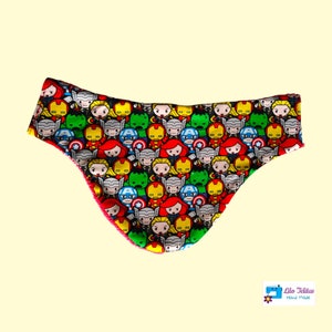Peut inclure: Un bavoir bébé en tissu rouge, vert et jaune avec un motif de super-héros de bande dessinée. Le bavoir est en forme de triangle incurvé et a une bordure rouge.