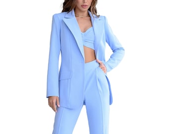 Puede incluir: Un traje de tres piezas azul claro, que incluye una blazer, un top corto y un pantalón. La blazer tiene solapas con muescas y bolsillos delanteros. El pantalón es de cintura alta. El conjunto se completa con tacones negros con tiras.
