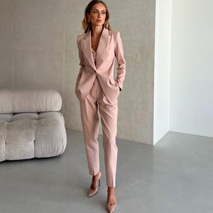 Può includere: Un completo pantalone rosa cipria con giacca e pantaloni abbinati. La giacca ha un revers a punta e una chiusura con un solo bottone. I pantaloni hanno una gamba dritta e una lunghezza crop.