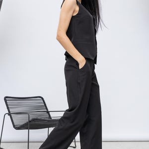 May include: A black sleeveless vest and wide-leg trousers suit. The outfit is paired with black and white patterned heels and large sunglasses. A black wire chair is in the background.
