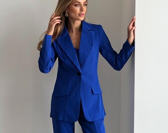 May include: A vibrant blue suit, featuring a tailored blazer with a single-button closure and two front pockets, paired with matching trousers. The suit is made of a smooth fabric and is a solid color. The outfit is a classic style.