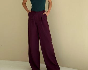 May include: A dark teal strapless corset top paired with wide-leg, pleated burgundy pants. The pants have a high waist and pockets. The outfit is a stylish ensemble, suitable for a variety of occasions.