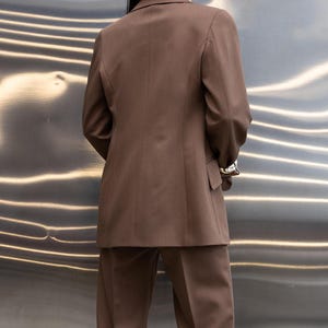 Pu&ograve; includere: Un completo marrone, composto da una giacca e pantaloni abbinati. La giacca ha un design classico con revers a lancia e chiusura a due bottoni. I pantaloni sono a gamba dritta. Il completo &egrave; realizzato in un tessuto liscio.
