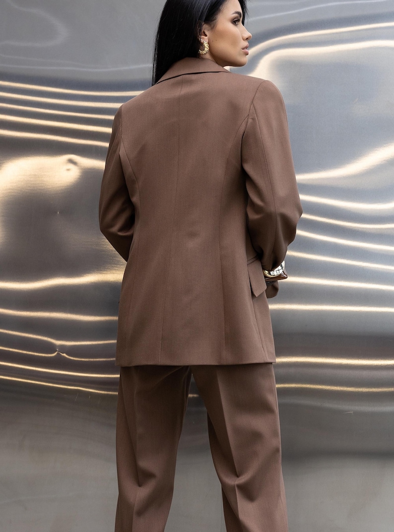 Pu&ograve; includere: Un completo marrone, composto da una giacca e pantaloni abbinati. La giacca ha un design classico con revers a lancia e chiusura a due bottoni. I pantaloni sono a gamba dritta. Il completo &egrave; realizzato in un tessuto liscio.