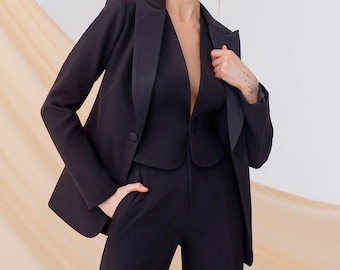 May include: A black three-piece suit consisting of a tailored blazer with satin lapels, a fitted vest with a deep V-neckline, and matching high-waisted trousers. The blazer features a single button closure and structured shoulders.