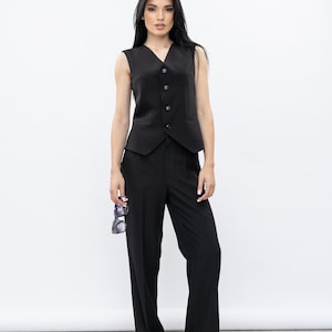 May include: A black waistcoat with a V-neck and button fastening, worn with matching black trousers. The outfit is finished with patterned shoes and sunglasses. The ensemble is a classic, tailored look.
