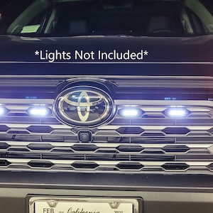 May include: A black Toyota RAV4 with a custom grille featuring a honeycomb pattern and a row of LED lights. The text "*Lights Not Included*" is visible above the grille.