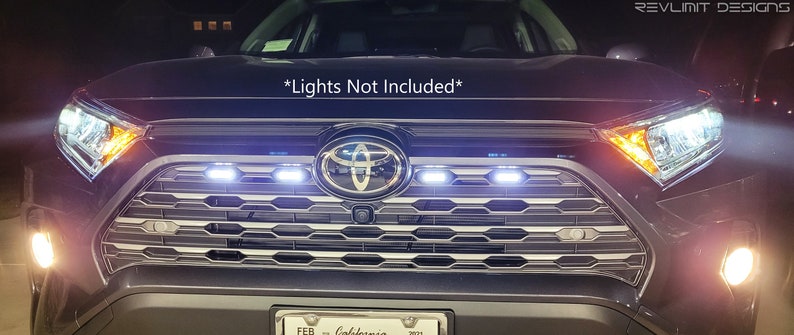 May include: A black Toyota RAV4 with a custom grille featuring a honeycomb pattern and a row of LED lights. The text "*Lights Not Included*" is visible above the grille.