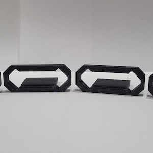 May include: Five black plastic 3D printed octagonal rings with a rectangular opening in the center.