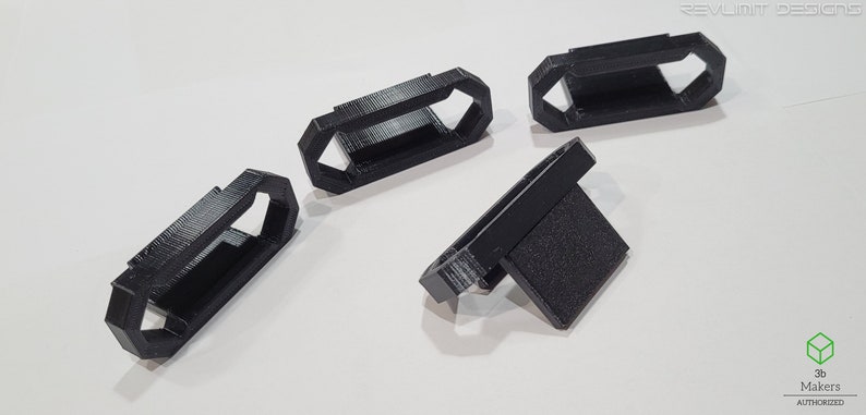 May include: Four black 3D printed plastic parts. Three of the parts are shaped like a rectangle with a hole in the middle. The fourth part is shaped like a rectangle with a small rectangular protrusion on one side.