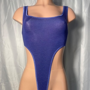 May include: A blue bodysuit with a high-cut leg and square neckline. The bodysuit is a solid color with a light blue trim around the edges. The garment is displayed on a mannequin.