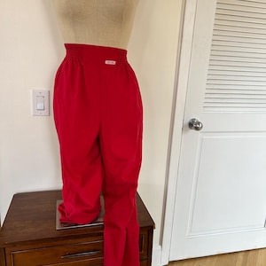 May include: Bright red high-waisted pants with an elastic waistband. The pants are displayed on a mannequin. The pants have a relaxed fit and a slight flare at the bottom. The pants are made of a smooth, lightweight fabric.