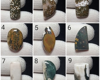 Könnte beinhalten: Neun polierte Edelsteine in verschiedenen Formen und Farben. Die Edelsteine umfassen rechteckige, ovale und tropfenförmige Formen. Die Farben reichen von Grün und Braun bis Weiß und Creme, mit einzigartigen Mustern und Texturen. Ideal für die Schmuckherstellung oder das Sammeln.