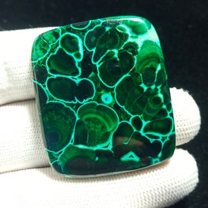 May include: A green and blue malachite cabochon with a swirling pattern. The stone is polished and has a smooth surface.