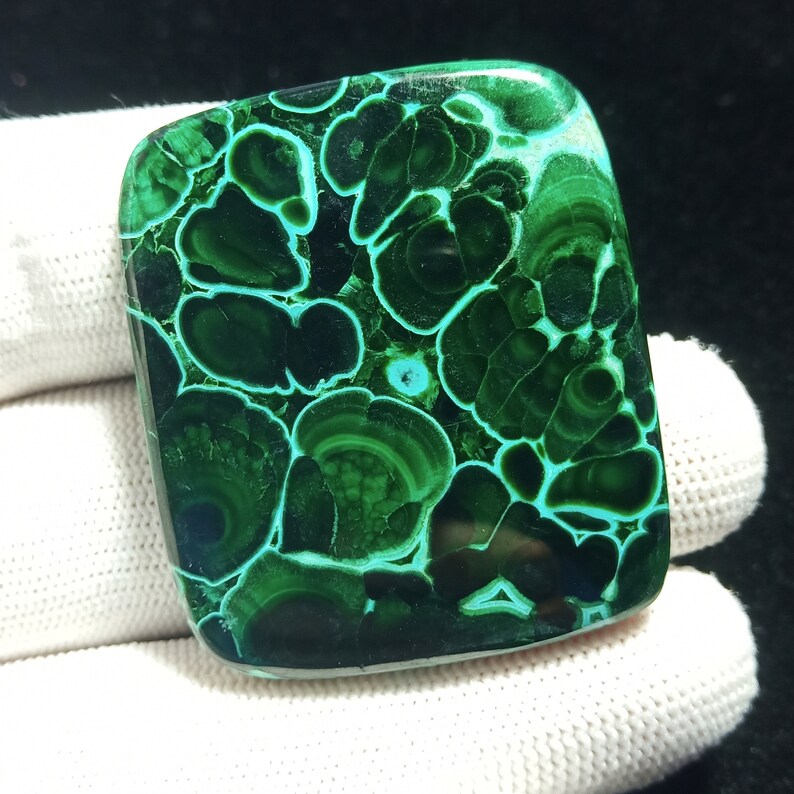 May include: A green and blue malachite cabochon with a swirling pattern. The stone is polished and has a smooth surface.