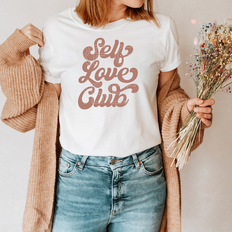 Puede incluir: Camiseta blanca con un gr&aacute;fico marr&oacute;n que dice "Self Love Club" en una fuente retro.