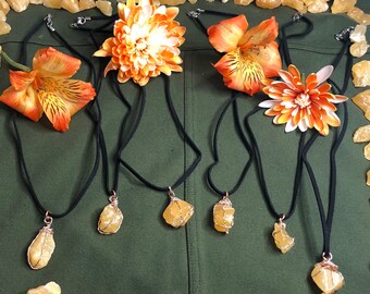 May include: Five necklaces with yellow crystal pendants on black cords. The necklaces are displayed on a green fabric background with yellow flowers.