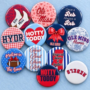 May include: A collection of eleven round pinback buttons featuring various designs related to Ole Miss. The buttons display text such as Hotty Toddy, Ole Miss, HYDR, Once a Reb Always a Reb, Meet me in the Grove, and Oxford does it better, alongside graphics of boots, a red bow, a football, and floral patterns.