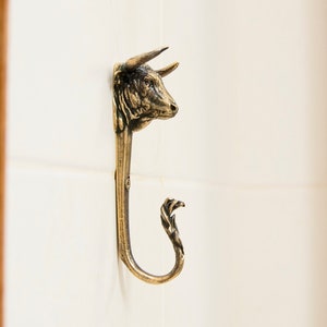 Op de afbeelding: Een messing haak in de vorm van een stierenkop met een decoratieve gekrulde staart.