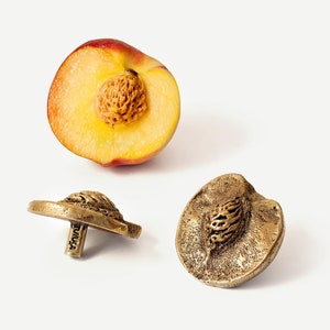 Pode incluir: Dois botões de metal dourados em forma de pêssego com um design de caroço detalhado. Os botões são mostrados ao lado de um pêssego cortado ao meio.