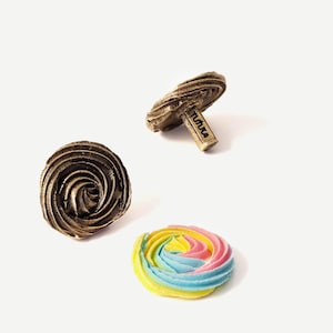 Könnte beinhalten: Zwei braune, spiralförmige, dekorative Keramikgegenstände und ein einzelnes, buntes, spiralförmiges Baiser.