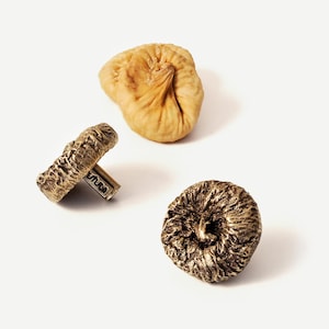 May include: Three dried figs, two are brown and one is a light brown color. The figs are on a white background.