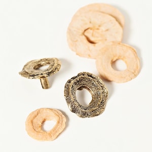 Op de afbeelding: Twee messingkleurige metalen ladegrepen met een getextureerd, organisch ontwerp. De grepen zijn ringvormig met een verhoogd midden.