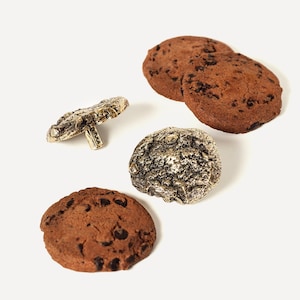 Puede incluir: Cuatro galletas con chispas de chocolate sobre un fondo blanco. Tres de las galletas son marrones y una es dorada.