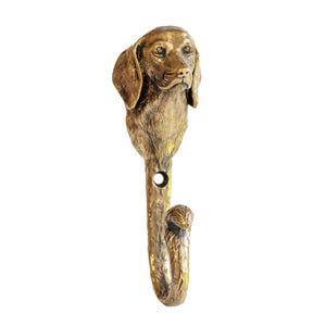 May include: A bronze-coloured metal wall hook, shaped like a dog's head. The hook has a detailed sculpture of a dog's face and a curved hook for hanging items. The dog's head is at the top of the hook, with a hole in the stem.