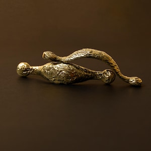 Peut inclure: Deux poignées de tiroir ou poignées en métal doré ornementales. Les poignées présentent un design texturé et organique, avec un centre bulbeux et des extensions courbes en forme de branche. Le fond est marron foncé.