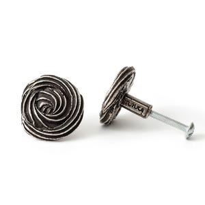 May include: Two round cabinet knobs with a dark, weathered silver finish. The front face of each knob features a raised, swirling spiral pattern that resembles a rose. A threaded metal bolt extends from the back of one knob for installation.