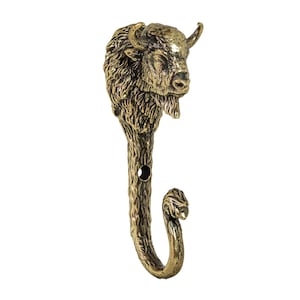 May include: A bronze-colored metal wall hook featuring a detailed bison head design. The hook has a curved lower portion and a small hole for mounting. The bison's fur and facial features are intricately sculpted.