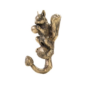 May include: A gold-toned metal squirrel hook with a mushroom base. The squirrel is holding a nut in its paws and is perched on top of the mushroom.