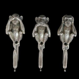 Può includere: Tre statuette di scimmia color argento nella posa 'non vedere, non sentire, non parlare'. Ogni scimmia è seduta su un lungo e sottile stelo. Lo sfondo è nero.