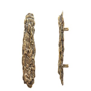 May include: Two bronze-colored door pulls with a textured, bark-like appearance. The pulls are vertical and have a rugged, natural aesthetic. One pull is shown from the front, the other from the side, both against a white background.