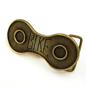 The "Bike" bicycle buckle, made of brass in the shape of a bicycle chain link, is perfect for all cycling enthusiasts.
