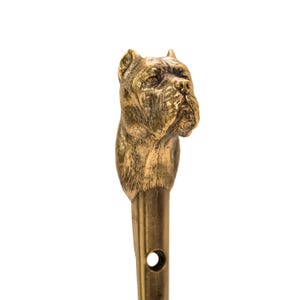 Op de afbeelding: Een gouden metalen haak met een gedetailleerd beeldhouwwerk van een hondenkop. De haak is ontworpen om items aan een muur te hangen.