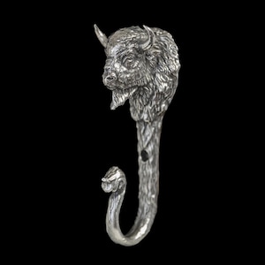 May include: A silver-colored metal wall hook featuring a detailed bison head at the top. The hook has a textured, tree-like stem and a curved hook at the bottom. The bison has horns and a detailed fur texture.