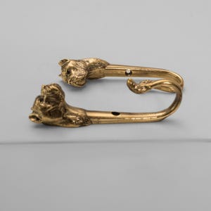 Op de afbeelding: Twee gouden metalen haken in de vorm van hondenkoppen. De haken zijn ontworpen om aan een muur te worden gemonteerd.