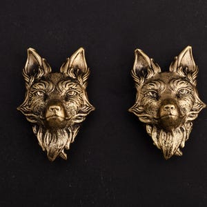 May include: Two gold-coloured fox head sculptures with detailed features, set against a black background.