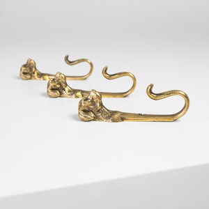 May include: Three gold-toned metal hooks shaped like a dog's head with a curled tail.