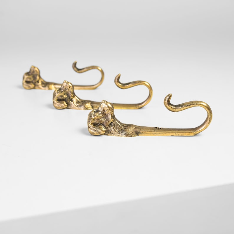 May include: Three gold-toned metal hooks shaped like a dog's head with a curled tail.