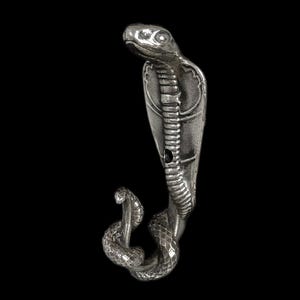 Op de afbeelding: Een zilverkleurig cobrafiguur met een gedetailleerd, gestructureerd ontwerp. De cobra staat rechtop, met zijn kap uitgespreid, en een kleinere cobra is aan de basis opgerold. De achtergrond is effen zwart.