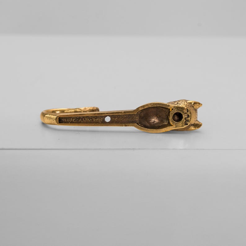 Op de afbeelding: Een gouden metalen haak in de vorm van een kat. De haak is gemaakt in Oekra&iuml;ne en heeft een klein gaatje aan de achterkant.