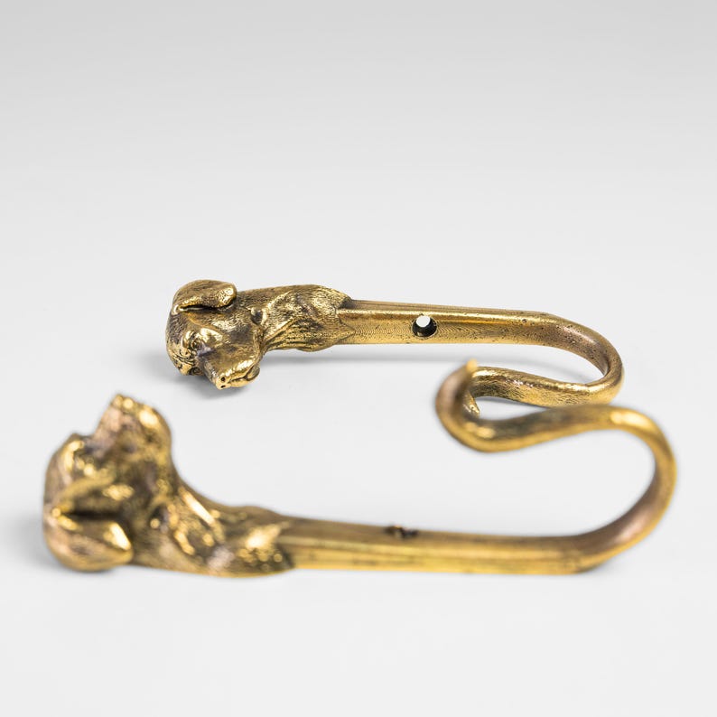 May include: Two gold-toned metal hooks shaped like a dog's head. The hooks are designed to be mounted on a wall.