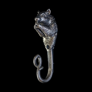 May include: A silver-toned bottle stopper featuring a detailed squirrel design at the top, holding something in its paws. The stopper has a curved, snake-like tail. The background is black.
